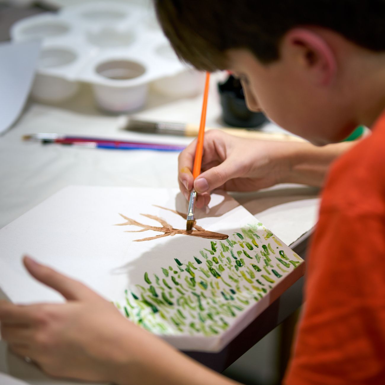 A young boy painting a tree on canvas