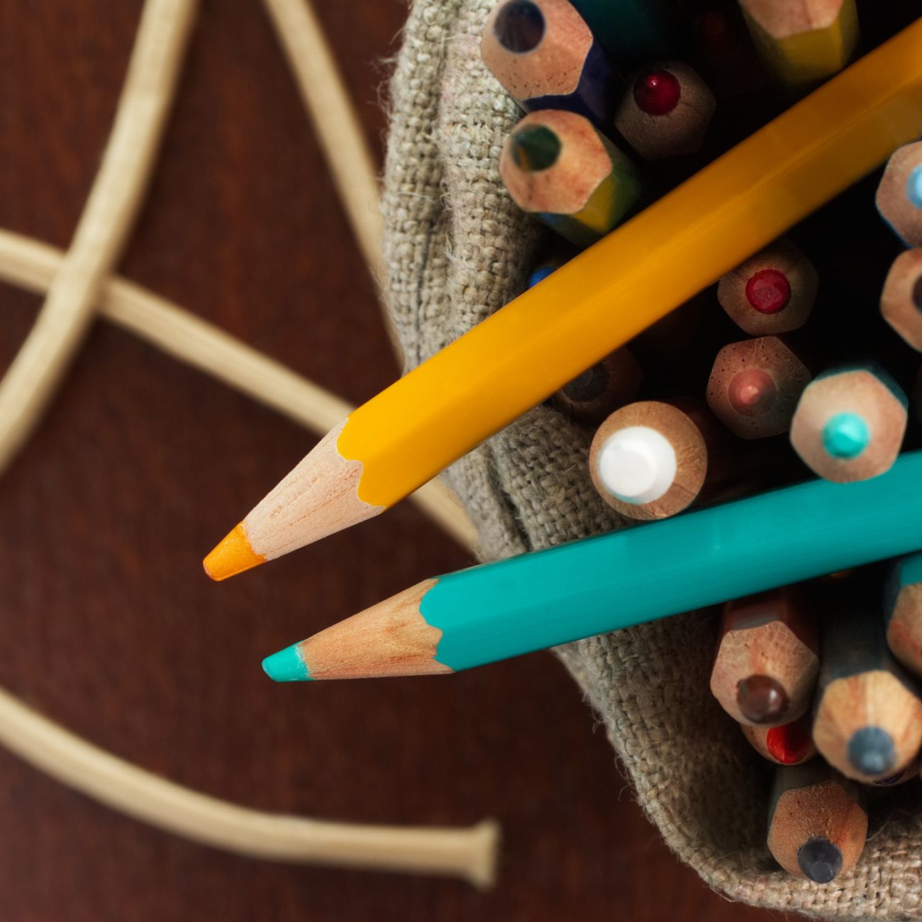 Colourful pencils in a jute sack on a wooden table