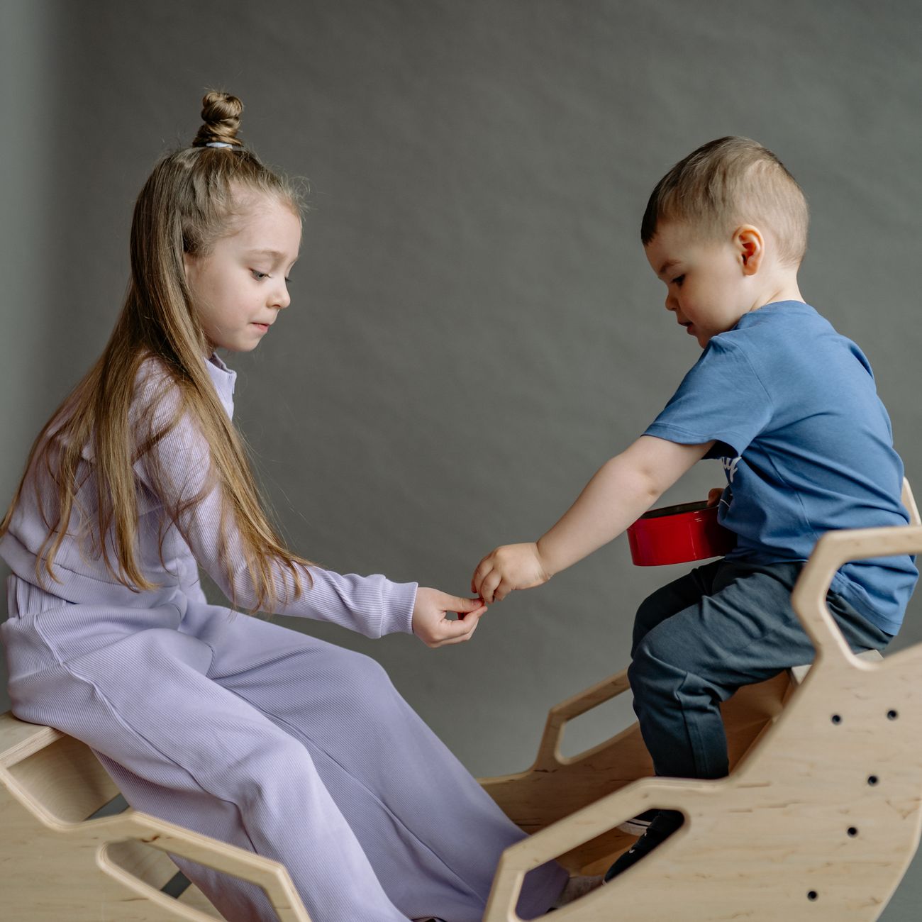 Two siblings sharing a moment on a wooden seesaw indoors